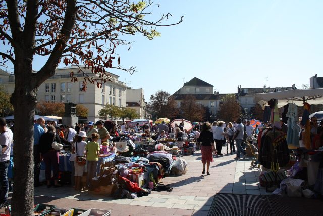 Brocante de Poissy Stands d’une brocante en plein air à Poissy, avec vêtements, jouets et objets d’occasion étalés sur des tables