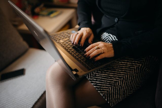 Une femme tape sur le clavier d’un ordinateur portable posé sur ses genoux